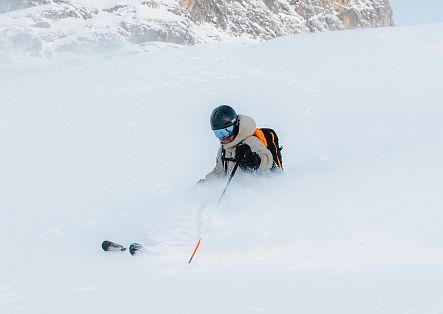 Ein Skifahrer taucht bei einer Fahrt durch tiefen Pulverschnee fast vollständig in einer Schneewolke unter.