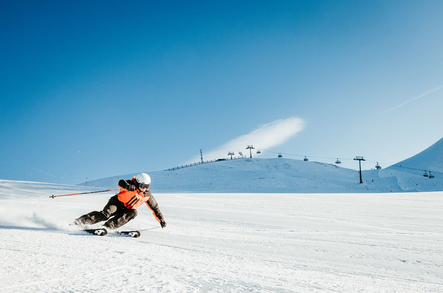Morgens zieht ein Skifahrer elegant die Abfahrt hinunter in Richtung Auenfeld, während die ersten Sonnenstrahlen die Piste beleuchten.