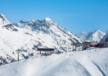 Verschneite Skipisten und Bergbahnen liegen vor einer beeindruckenden alpinen Bergkulisse.