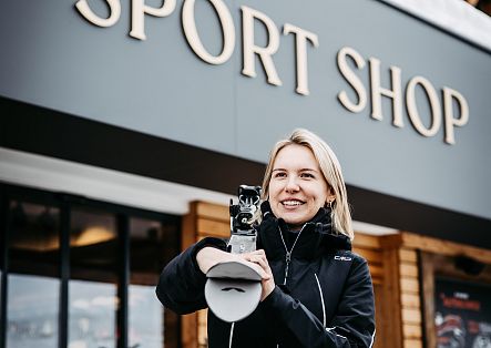Eine Frau steht vor einem Sportgeschäft und präsentiert einen Ski.