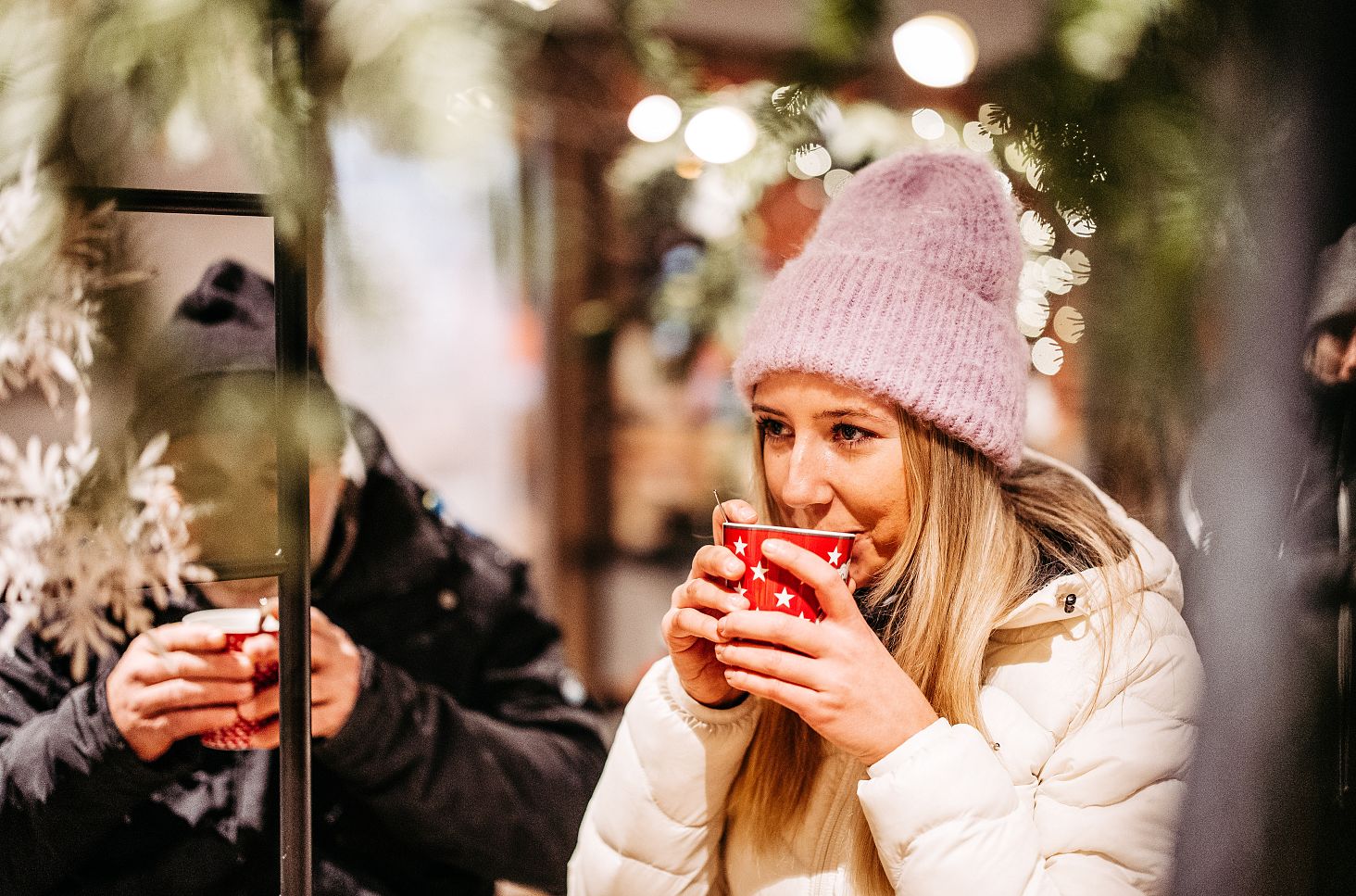Eine Person schlürft Glühwein aus einer roten Tasse in adventlicher Umgebung.