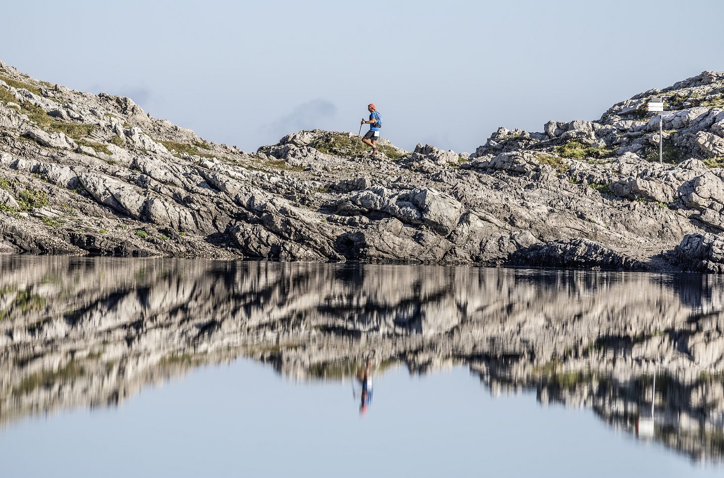 Ein Wanderer bewegt sich durch eine felsige Gebirgslandschaft, während sich die Szenerie beeindruckend im ruhigen Wasser eines Bergsees spiegelt.