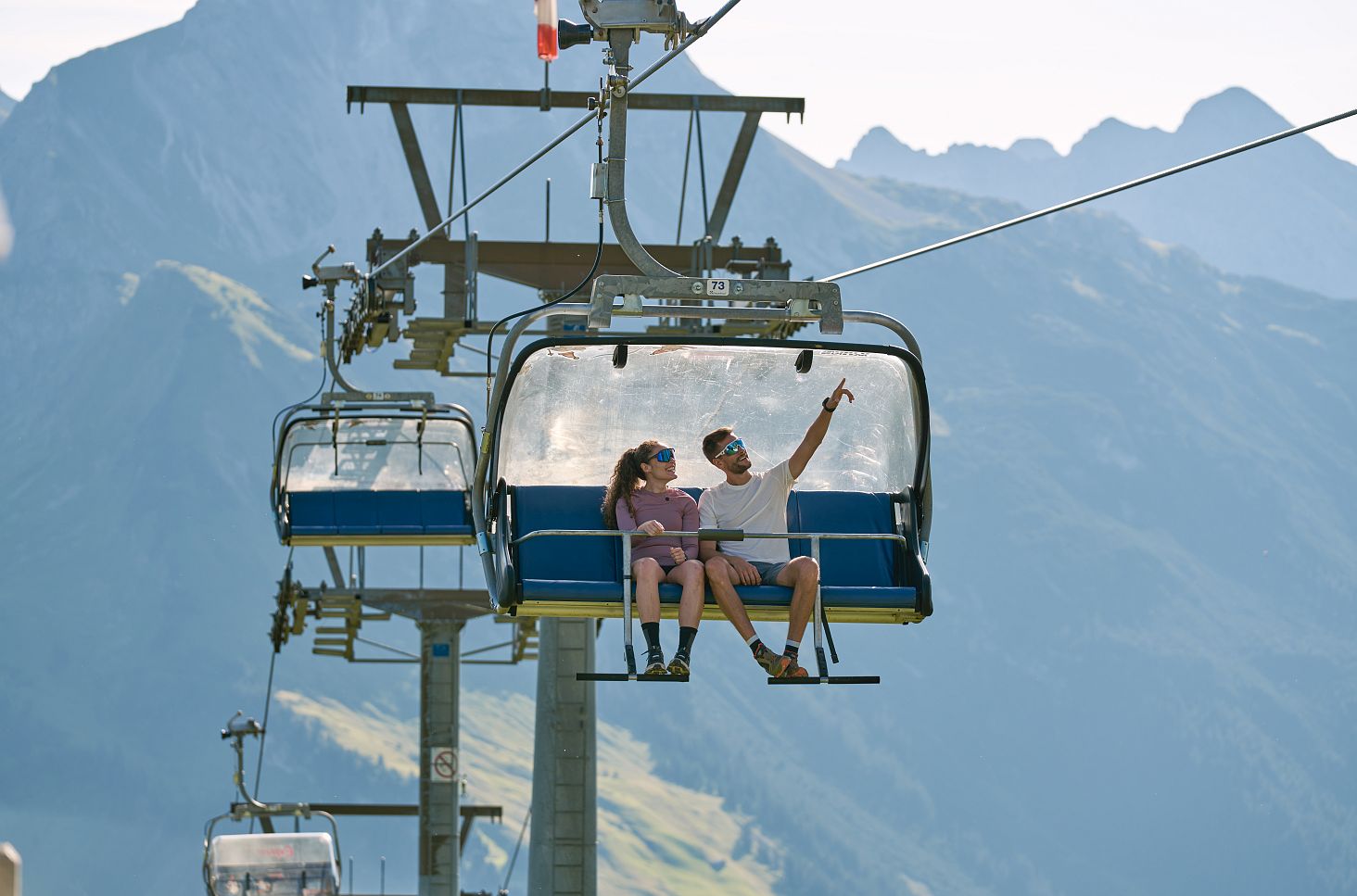Ein Paar fährt mit dem Sessellift Steffisalp-Express hoch, genießt die Aussicht und zeigt auf die umliegende Landschaft.